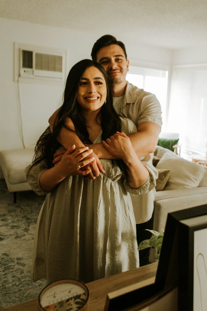 A smiling couple at home, the man embracing his partner from behind
