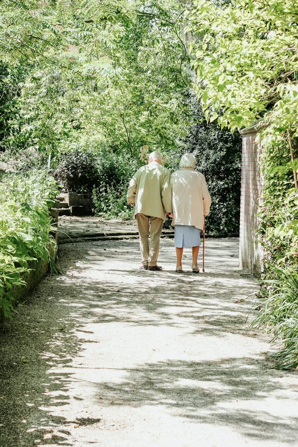 An older couple walking side by side along a sunlit garden path
