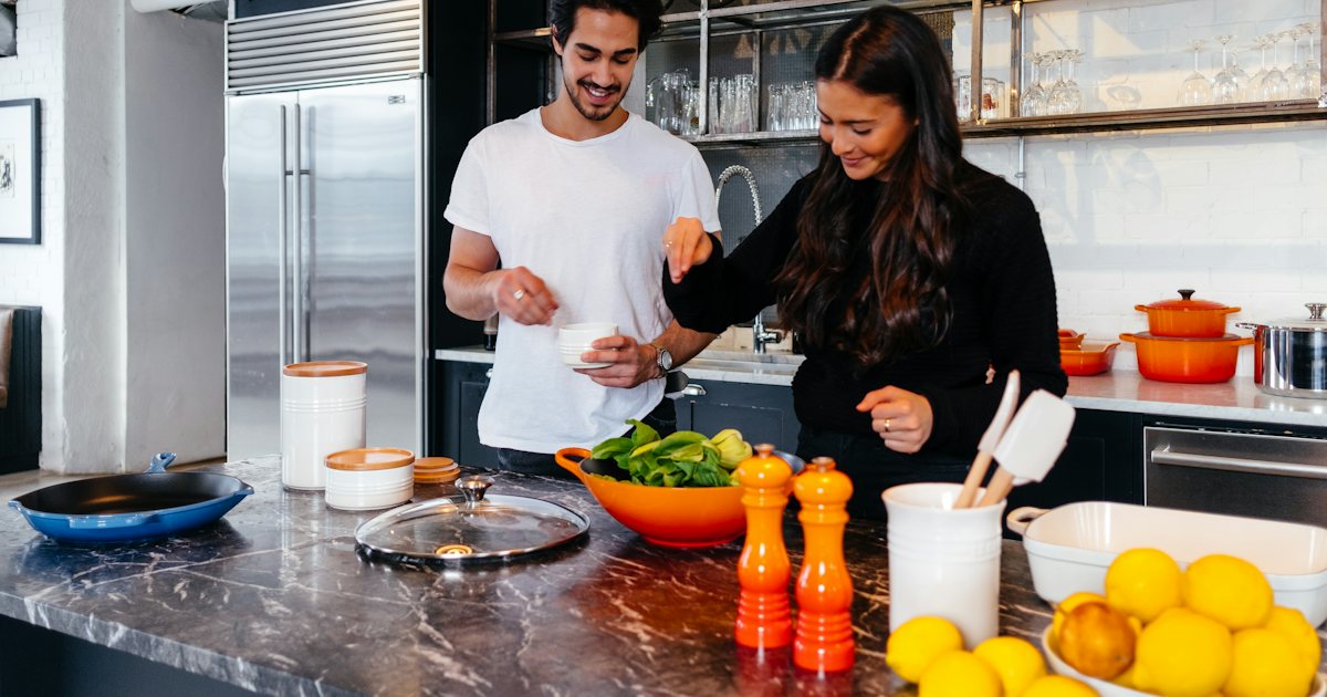 A couple smiling while cooking together in a bright kitchen
